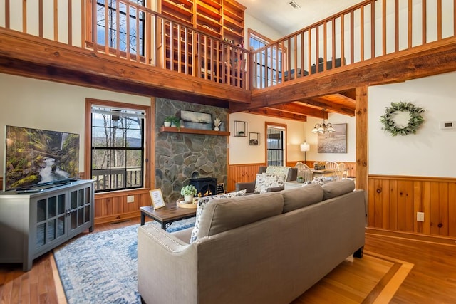 living room with wainscoting, a towering ceiling, a stone fireplace, wood finished floors, and a chandelier