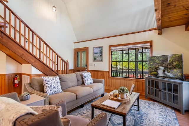 living area with a wainscoted wall, stairs, wood finished floors, wood walls, and beamed ceiling