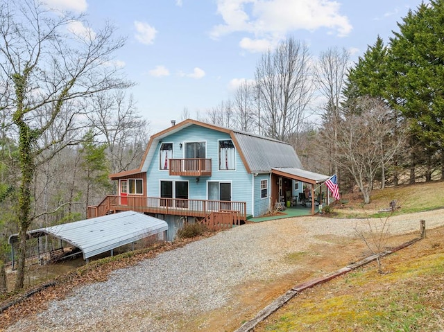 back of property with an attached carport, a gambrel roof, metal roof, a balcony, and driveway