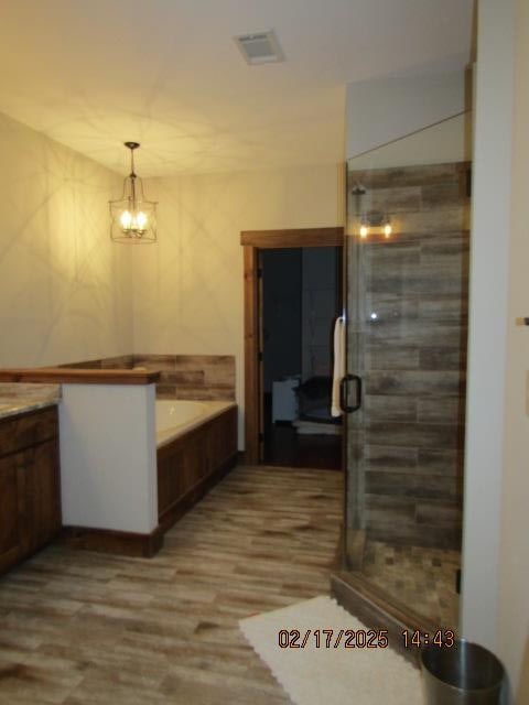 bathroom featuring hardwood / wood-style flooring, vanity, plus walk in shower, and a chandelier