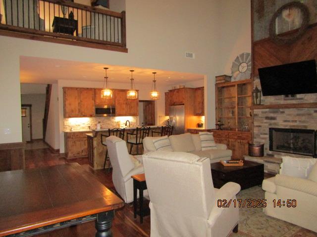 living room featuring a high ceiling, a stone fireplace, and dark hardwood / wood-style flooring