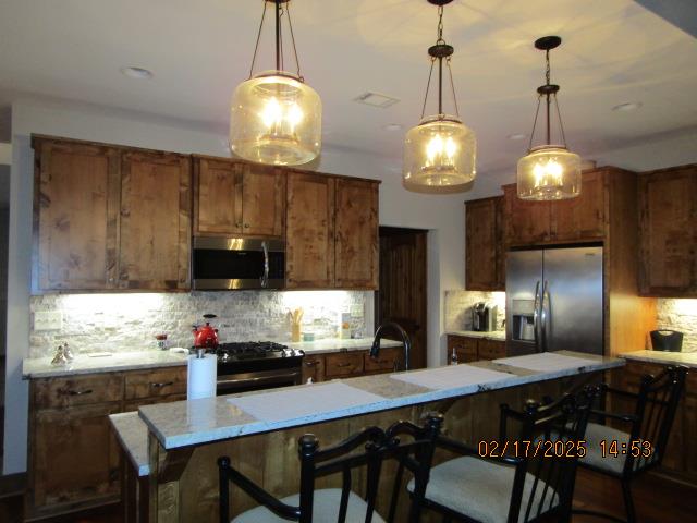 kitchen with hanging light fixtures, a center island, appliances with stainless steel finishes, and a kitchen breakfast bar