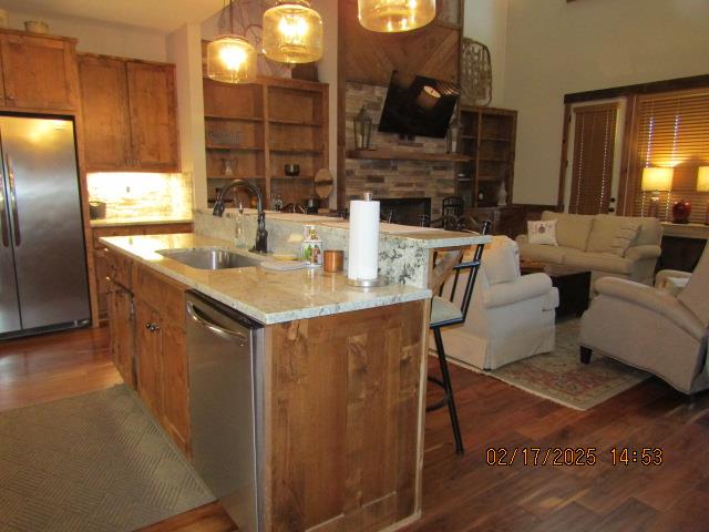 kitchen featuring stainless steel appliances, decorative light fixtures, sink, dark wood-type flooring, and a kitchen bar