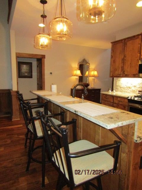 kitchen featuring dark hardwood / wood-style floors, hanging light fixtures, a breakfast bar area, and decorative backsplash