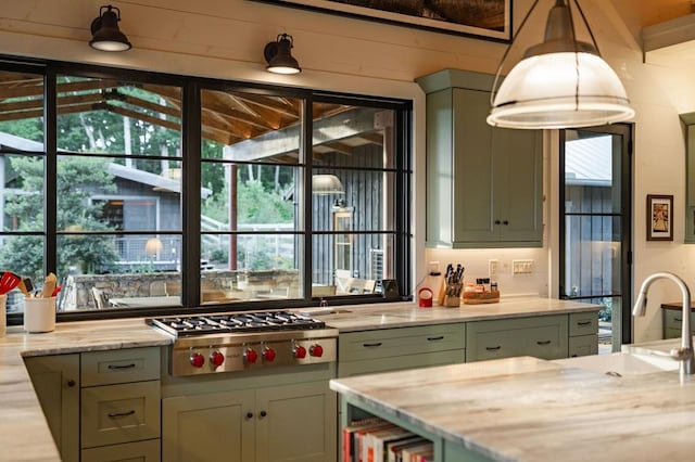 kitchen with light stone counters, a sink, hanging light fixtures, stainless steel gas stovetop, and green cabinets