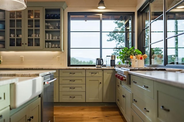 kitchen with hanging light fixtures, light countertops, glass insert cabinets, and light wood-style floors