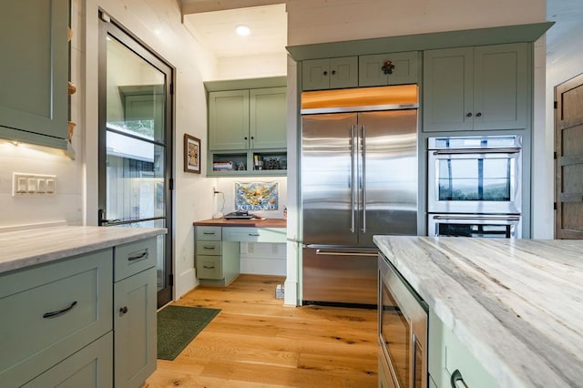 kitchen featuring green cabinets, light stone countertops, light wood-type flooring, and built in appliances