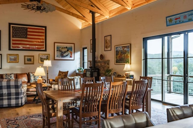 dining space with beam ceiling, a wood stove, wood finished floors, and wood ceiling