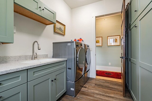 clothes washing area with a sink, washing machine and dryer, dark wood finished floors, cabinet space, and baseboards