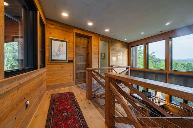 corridor with an upstairs landing, wood walls, wooden ceiling, and light wood-style floors