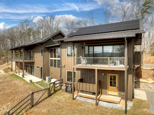 back of property with roof mounted solar panels, a patio, metal roof, and a balcony