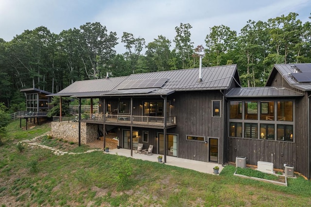 back of house with a yard, a patio, solar panels, and a standing seam roof