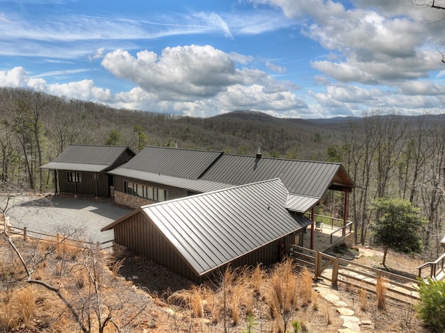 view of side of property with a wooded view, metal roof, a standing seam roof, and fence