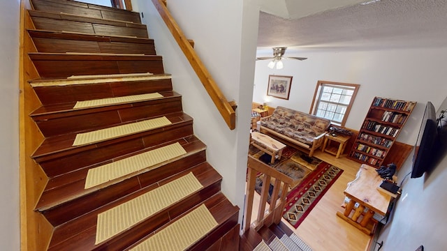 staircase with hardwood / wood-style floors, a textured ceiling, and ceiling fan