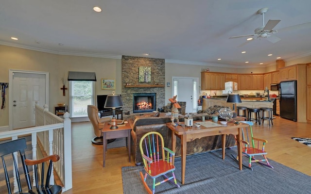 living room with crown molding, ceiling fan, a fireplace, and light hardwood / wood-style flooring