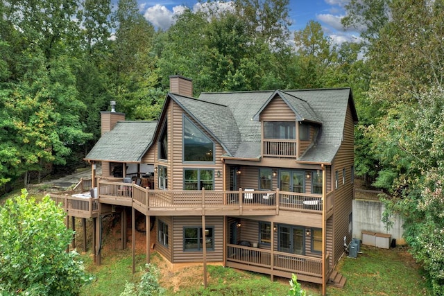 rear view of house featuring faux log siding, central air condition unit, roof with shingles, a deck, and a chimney