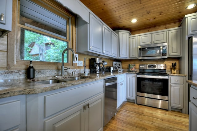 kitchen featuring appliances with stainless steel finishes, a sink, light wood-type flooring, light stone counters, and wooden ceiling