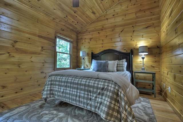 bedroom with light wood-style flooring, vaulted ceiling, and wood walls