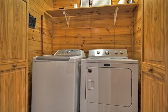 clothes washing area featuring washer and clothes dryer, wooden walls, and laundry area