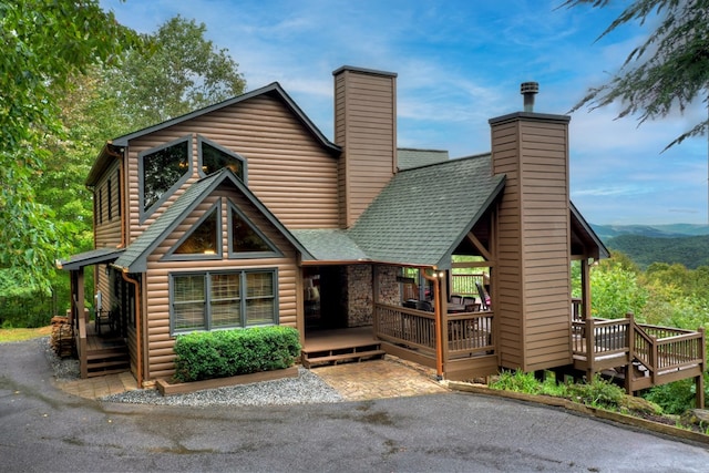 view of front facade with a shingled roof, a chimney, a wooden deck, and log veneer siding