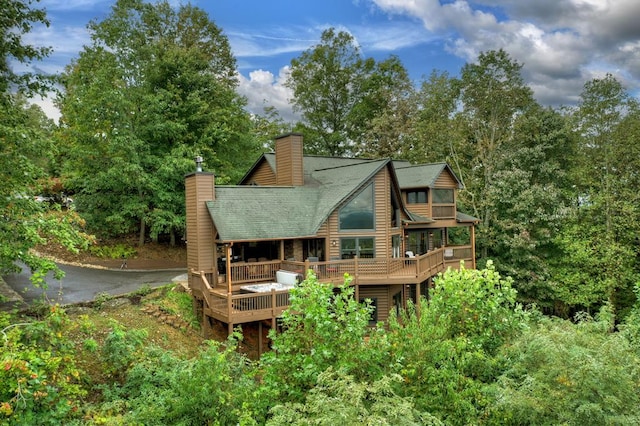 rear view of property featuring aphalt driveway, a chimney, a wooden deck, and log veneer siding