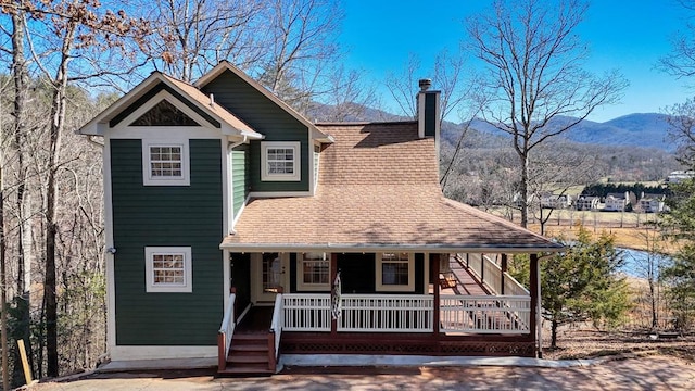 view of front of house with covered porch, a shingled roof, a chimney, and a mountain view