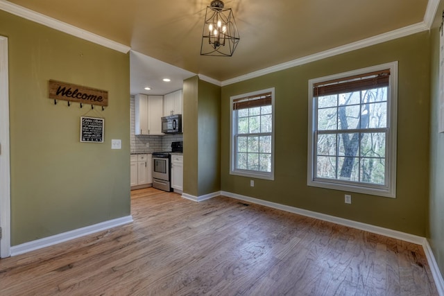 unfurnished dining area featuring crown molding, light wood finished floors, baseboards, and an inviting chandelier