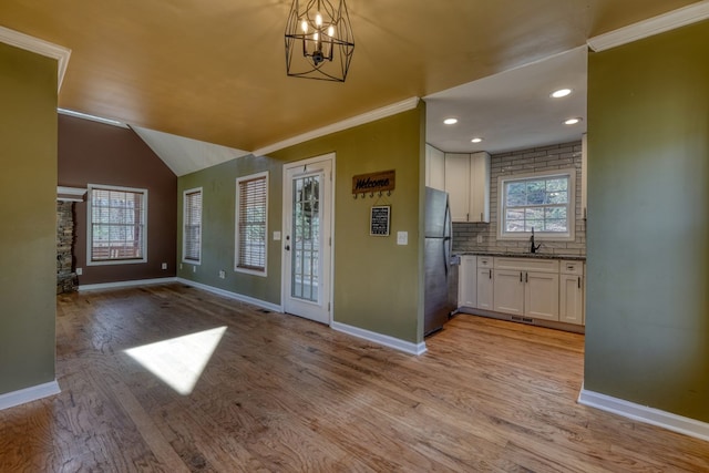 interior space with baseboards, light wood-style flooring, ornamental molding, vaulted ceiling, and a notable chandelier