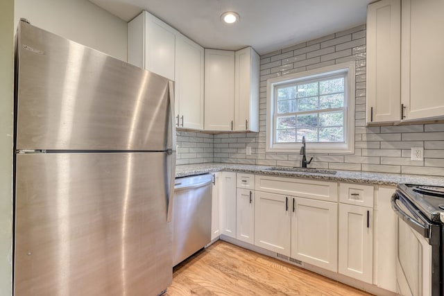 kitchen with stainless steel appliances, backsplash, a sink, and white cabinetry