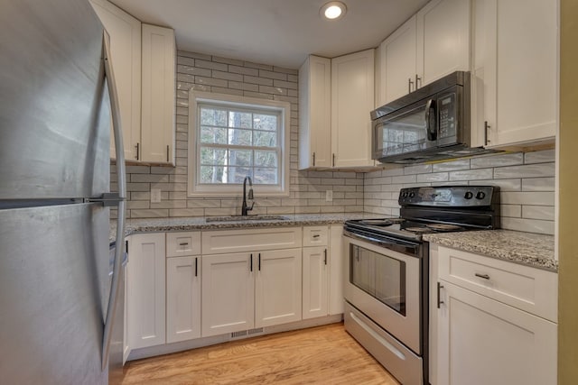 kitchen featuring decorative backsplash, stainless steel appliances, light wood-type flooring, white cabinetry, and a sink