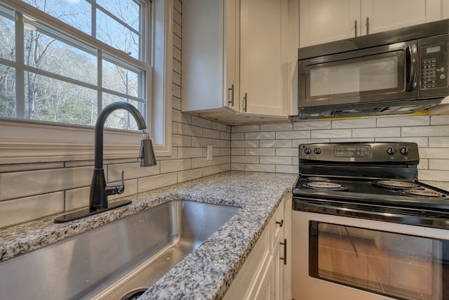 kitchen with black microwave, light stone counters, a sink, decorative backsplash, and stainless steel range with electric stovetop