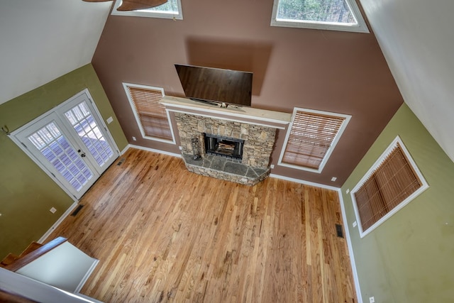 unfurnished living room featuring a towering ceiling, visible vents, wood finished floors, and a stone fireplace