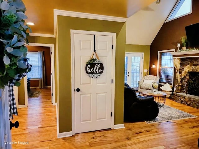 entrance foyer featuring lofted ceiling, light wood-style floors, baseboards, and a stone fireplace