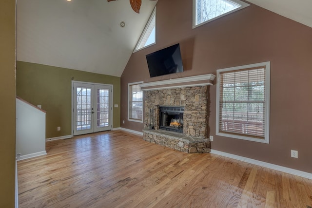 unfurnished living room featuring baseboards, french doors, wood finished floors, a stone fireplace, and high vaulted ceiling