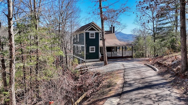 view of front facade featuring a porch, a chimney, and aphalt driveway