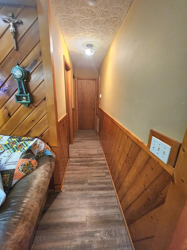 hall featuring wood-type flooring, a textured ceiling, and wood walls