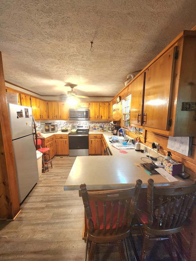 kitchen featuring appliances with stainless steel finishes, backsplash, a kitchen bar, light hardwood / wood-style floors, and kitchen peninsula