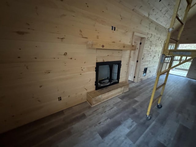 unfurnished living room with lofted ceiling, wood walls, a tiled fireplace, and wood finished floors