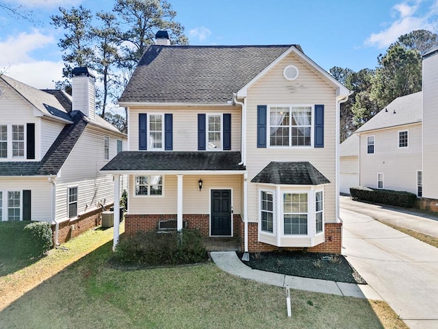 view of front of property with brick siding, a chimney, central air condition unit, a front yard, and driveway