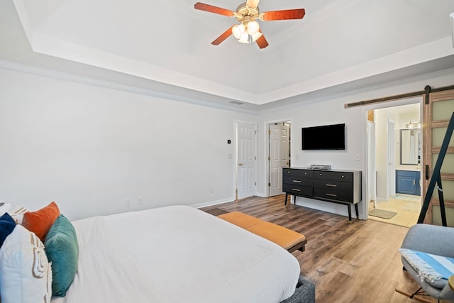 bedroom featuring a barn door, wood finished floors, baseboards, ornamental molding, and a tray ceiling