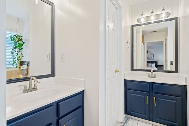 ensuite bathroom featuring crown molding, two vanities, and a sink