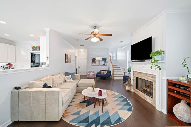 living area featuring stairs, a stone fireplace, wood finished floors, and crown molding