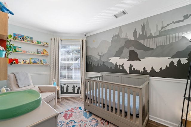 bedroom with a crib, visible vents, wood finished floors, and ornamental molding