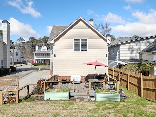 rear view of property with a vegetable garden, a chimney, a yard, fence, and a wooden deck