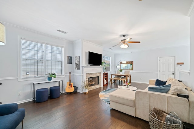 living room featuring a fireplace, visible vents, a ceiling fan, ornamental molding, and dark wood finished floors