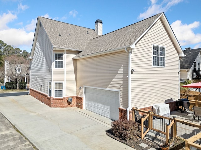 exterior space with concrete driveway, brick siding, a chimney, and roof with shingles