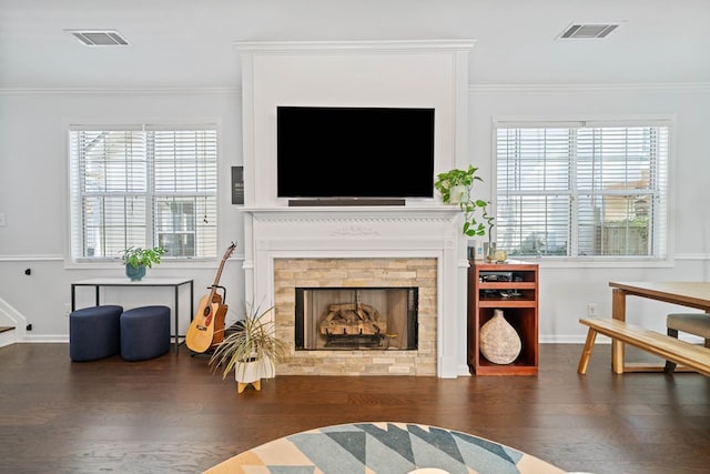 living area with a wealth of natural light, wood finished floors, visible vents, and crown molding