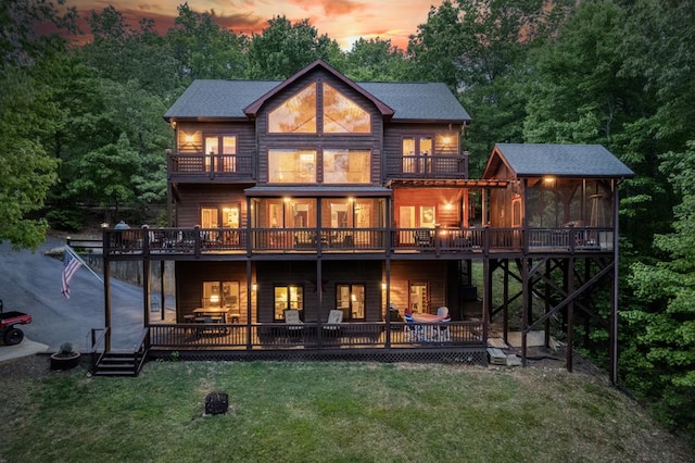 back house at dusk featuring a lawn, a sunroom, a balcony, and a deck