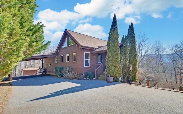 exterior space with driveway, an attached carport, and a shingled roof