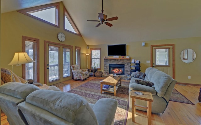 living room with high vaulted ceiling, a stone fireplace, ceiling fan, and light wood-style flooring